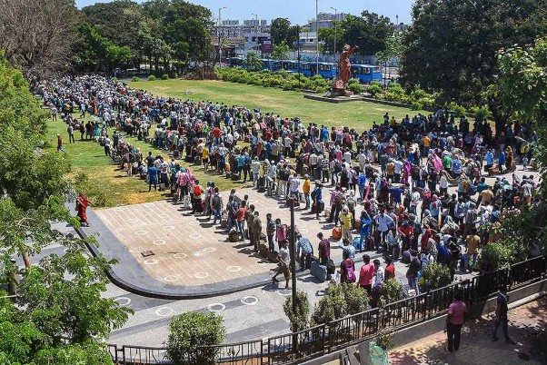सूरत में लॉकडाउन के दौरान अपने मूल स्थानों तक पहुंचने के लिए रेलवे स्टेशन जाने के लिए बसों का इंतजार करते प्रवासी श्रमिक