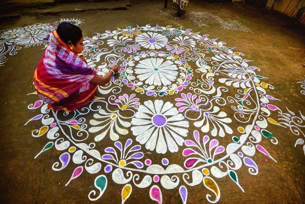 अगरतला के बाहरी इलाके स्थित एक गांव में मकर संक्रांति के मौके पर अपने घर के सामने 'रंगोली' बनाती महिला