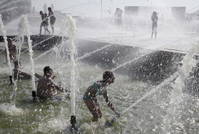 रूस के सेंट पीटर्सबर्ग में गर्मी से राहत पाने फव्वारे पर नहाते लोग