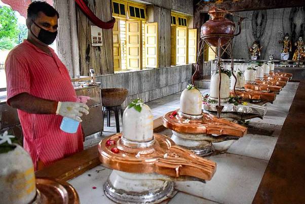 प्रयागराज में 'सावन' के पवित्र महीने के पहले सोमवार के अवसर पर एक मंदिर के अंदर 'शिवलिंग' को सैनिटाइज करता पुजारी