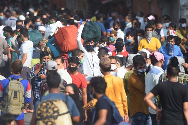 मुंबई में लॉकडाउन के दौरान रेलवे स्टेशन तक पहुंचने के लिए धारावी झुग्गी बस्ती के बाहर बसों का इंतजार करते प्रवासी श्रमिक