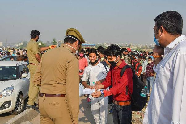 नई दिल्ली में चल रहे लॉकडाउन के दौरान दिल्ली-यूपी सीमा में प्रवेश करने के लिए एक पुलिस अधिकारी को ट्रेन का टिकट दिखाता प्रवासी श्रमिक
