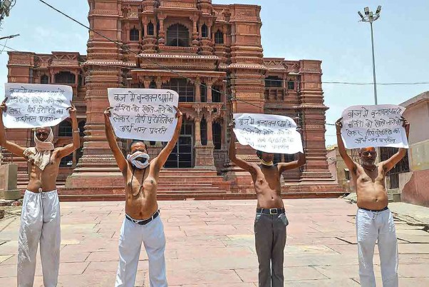 कोरोना के चलते लगाए गए लॉकडाउन के बीच वृंदावन में हाथों में तख्तियां लिए मंदिरों को खोलने की मांग करते लोग