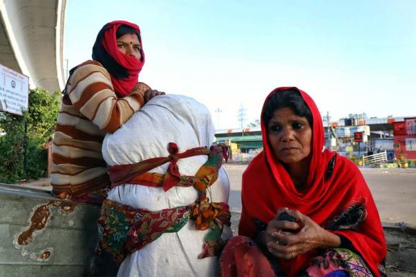 देशव्यापी तालाबंदी के बीच सामान लिए आनंद विहार बस अड्डे पर गांव जाने की आस में बैठी महिला