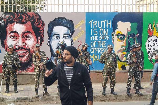 जामिया मिलिया इस्लामिया विश्वविद्यालय के बाहर नागरिकता संशोधन कानून के विरोध में बने चित्रों के सामने खड़े सुरक्षाकर्मी