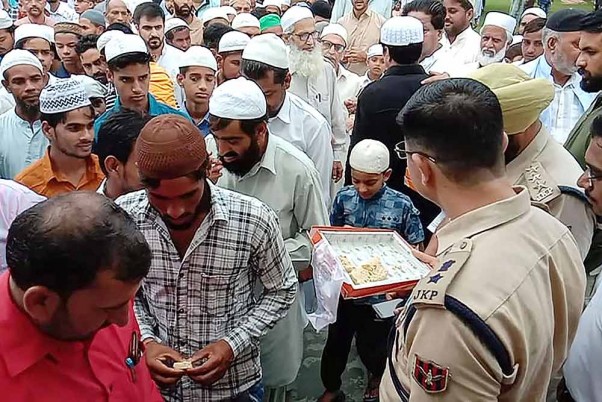 श्रीनगर में ईद-उल-अजहा की नमाज अदा करने के बाद पुलिस अधिकारी लोगों को मिठाई खिलाते हुए