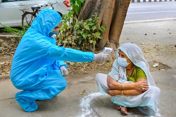 राजधानी दिल्ली में लॉकडाउन के दौरान खाना लेने के लिए कतार में इंतजार करती एक बुजुर्ग महिला की थर्मल स्कैनिंग करता एक अधिकारी