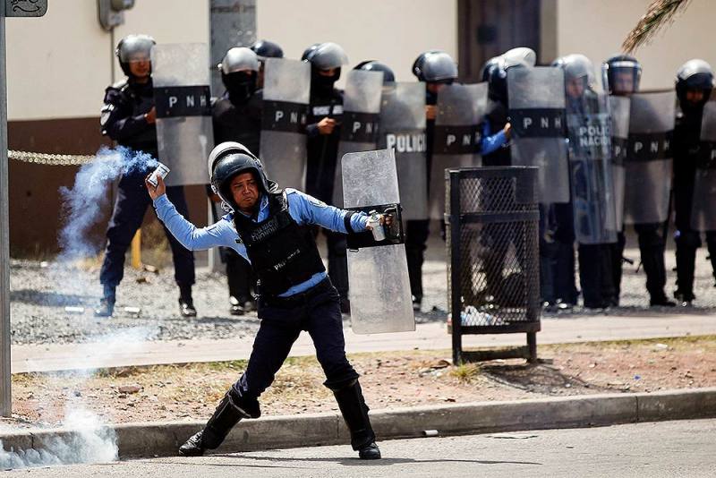 टेगुसिगलपा में राष्ट्रपति हर्नांडेज की सरकार के खिलाफ प्रदर्शनकारियों पर आंसू गैस का गोला फेंकते पुलिस अधिकारी।