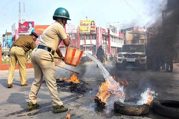 अगरतला में नागरिकता संशोधन कानून  के खिलाफ हड़ताल के दौरान प्रदर्शनकारियों द्वारा जलाए गए टायर को बुझाते पुलिसकर्मी