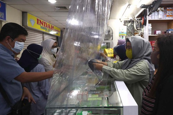 इंडोनेशिया के जकार्ता में फार्मेसी शॉप पर कोरोना के संक्रमण से बचने के लिए प्लास्टिक शीट का सहारा लेती विक्रेता