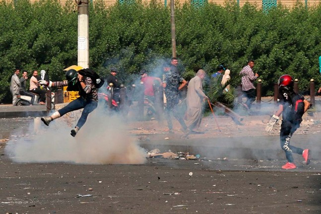 इराक की राजधानी बगदाद में विरोध प्रदर्शन के दौरान आंसू गैस के गोले से बचते प्रदर्शनकारी