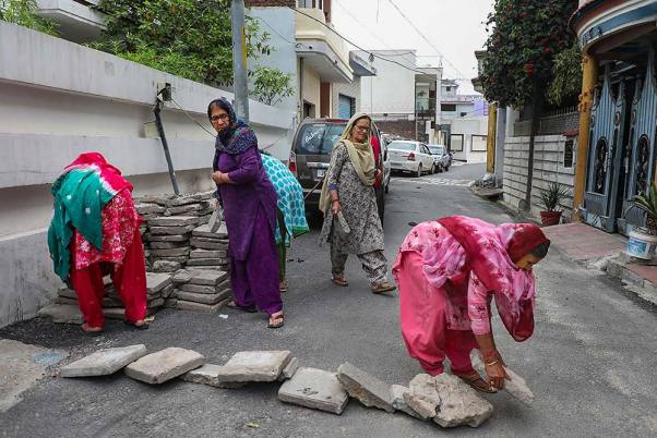 जम्मू में शक्ति नगर की कॉलोनियों में आगंतुकों के आने-जाने पर रोक लगाने के लिए सड़कों पर पत्थर रखकर जाम करती महिलाएं
