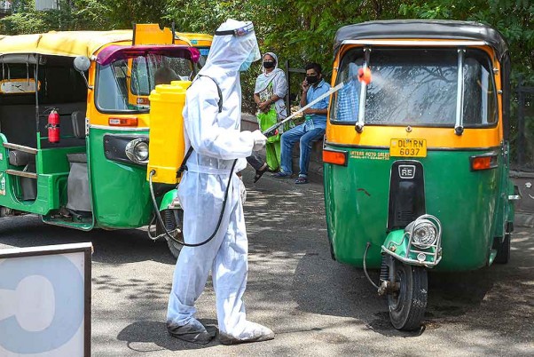 राजधानी दिल्ली में लॉकडाउन के दौरान पीपीई किट पहनकर ऑटो-रिक्शा पर कीटाणुनाशक का छिड़काव करता कर्मचारी
