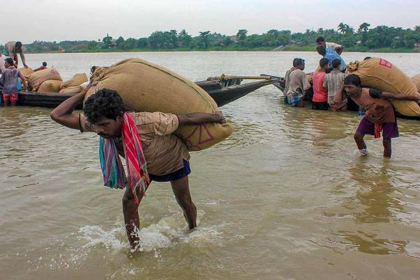 बाजार में बेचे जाने के लिए पश्चिम बंगाल के नादिया जिले में नाव से चावल की बोरी ढोते श्रमिक।