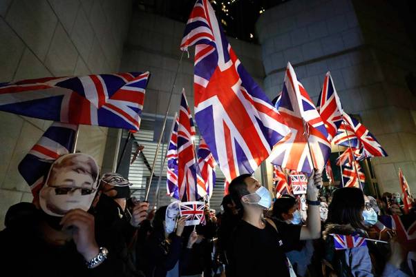 हांगकांग में ब्रिटिश वाणिज्य दूतावास के बाहर रैली के लिए हाथ में झंडा लिए इकट्ठा हुए प्रदर्शनकारी