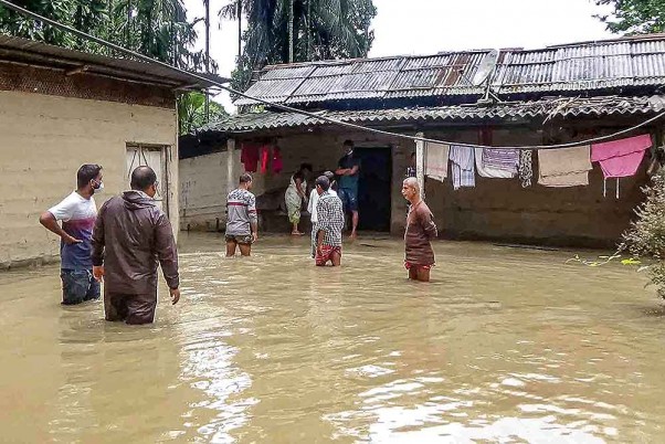 असम के नलबाड़ी जिले में बाढ़ प्रभावित गांव में अपने घर के बाहर खड़े लोग