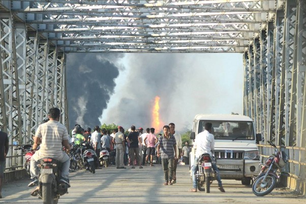 असम के तिनसुकिया के बागजान तेल कुआं में लगी भीषण आग से उठते धुंए को देखने पहुंचे आसपास के लोग