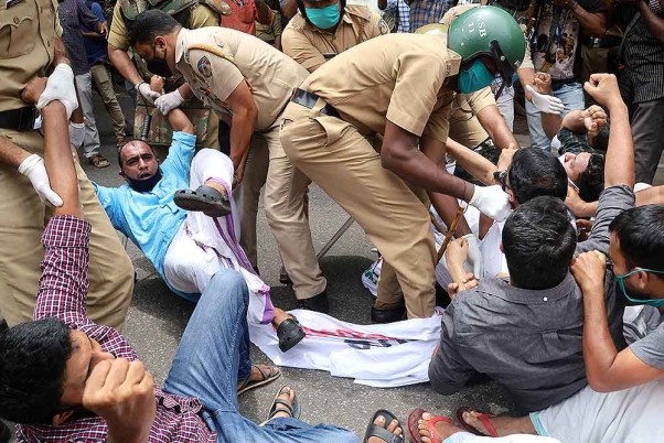 कोविड-19 टेस्ट के बाद एनआरआई को केरल में प्रवेश की अनुमति देने के राज्य सरकार के फैसले के विरोध में सड़कों पर उतरे यूथ लीग के कार्यकर्ताओं को हिरासत में लेते पुलिसकर्मी