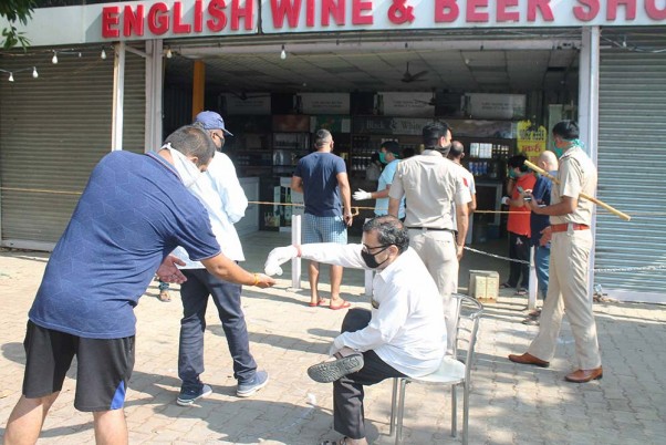 फरीदाबाद में लॉकडाउन के तीसरे चरण के दौरान खोली गई शराब की दुकान के बाहर लाइन में खड़े लोगों के हाथों को सेनिटाइज करवाता एक आदमी