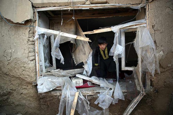 अफगानिस्तान के काबुल के परवन प्रांत में बगराम एयर बेस के पास एक हमले के बाद अपने क्षतिग्रस्त घर से बाहर देखता किशोर