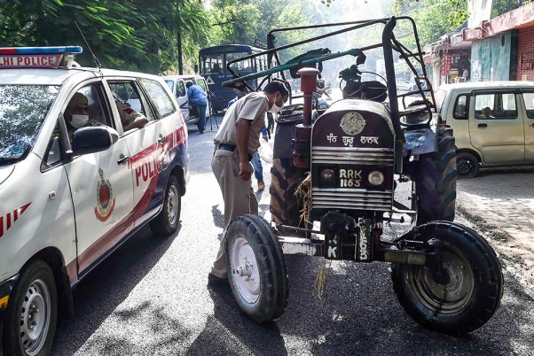 नई दिल्ली में नए कृषि कानून के खिलाफ प्रदर्शन के दौरान इंडिया गेट के पास आग लगने के बाद तिलक मार्ग पुलिस स्टेशन में ट्रैक्टर का निरीक्षण करता एक पुलिसकर्मी