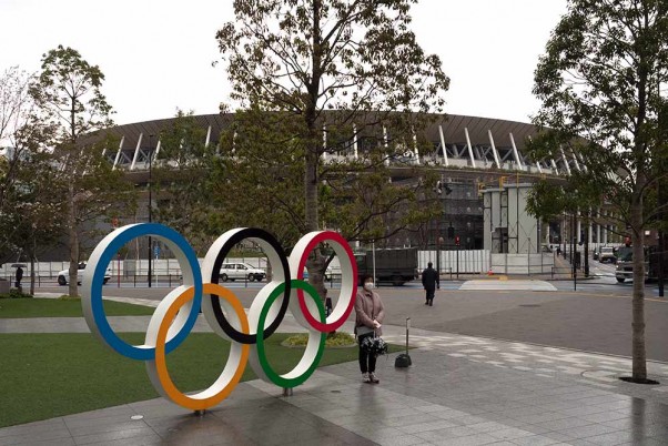 टोक्यो के न्यू नेशनल स्टेडियम के पास ओलंपिक रिंग के बगल में खड़े होकर मास्क लगाकर फोटो खिंचवाती एक महिला
