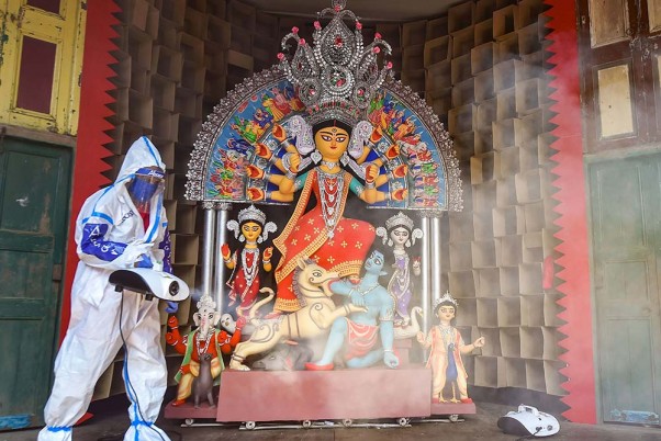 कोलकाता में दुर्गा पूजा उत्सव से पहले पीपीई किट पहनकर एक पूजा पंडाल को सेनिटाइज करता कर्मचारी