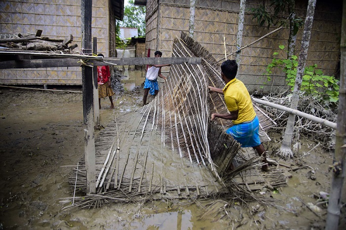 असम के मोरीगांव जिले के बाढ़ प्रभावित बोगोलीपारा गांव में क्षतिग्रस्त झोपड़ी को दोबारा तैयार करने में जुटा एक परिवार