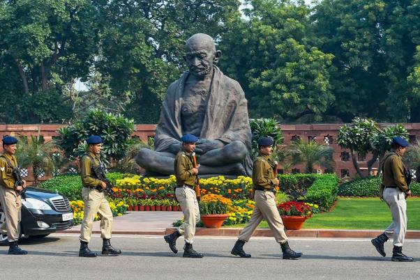 शीतकालीन सत्र के दौरान संसद भवन में महात्मा गांधी की प्रतिमा के सामने चलते सुरक्षाकर्मी