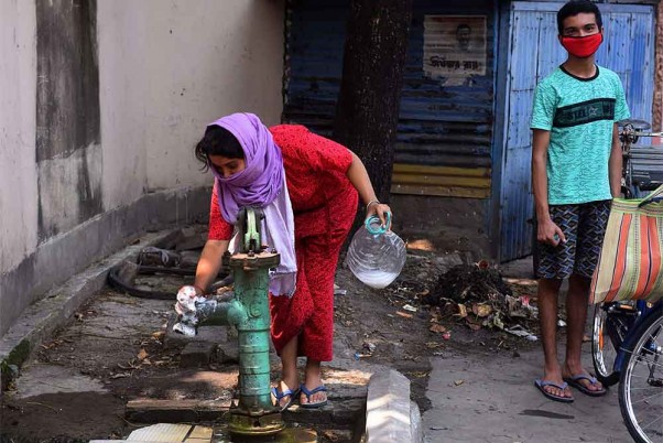 कोरोना वायरस महामारी के मद्देनजर लॉकडाउन के दौरान पश्चिम बंगाल में पानी लेने से पहले हैण्डपंप को सेनिटाइज करती महिला