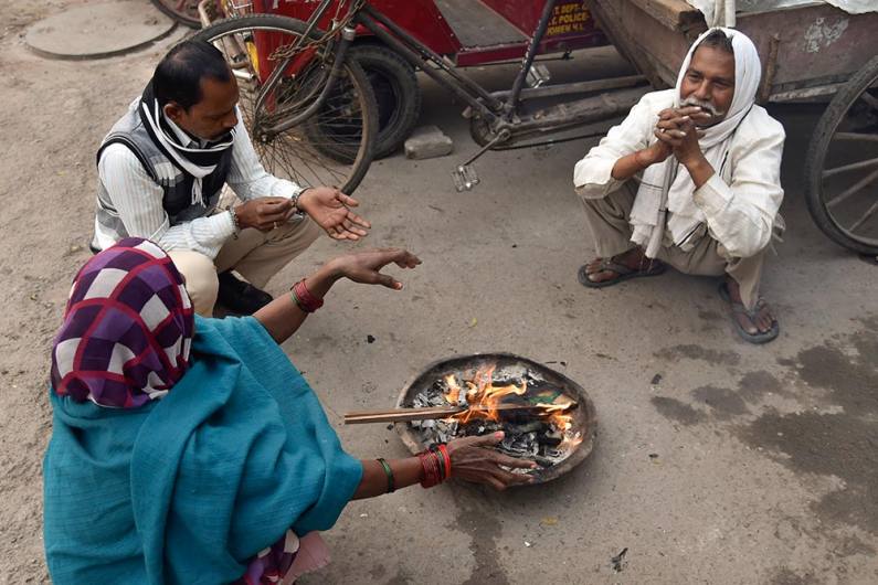 नई दिल्ली की सुर्द सुबह से राहत पाने आग के पास बैठे लोग
