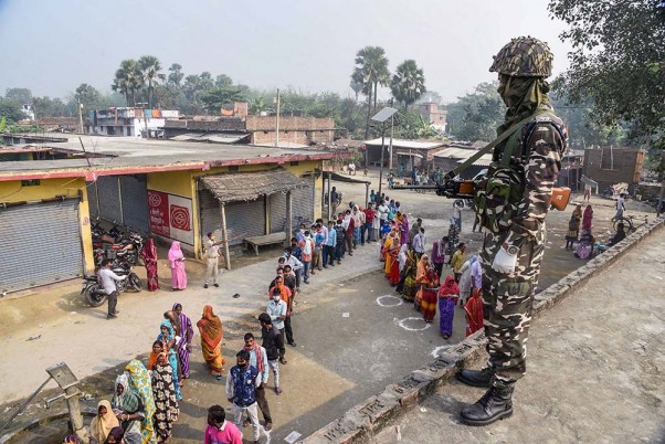 बिहार चुनाव के तीसरे चरण के दौरान एक मतदान केंद्र पर सुरक्षा के बीच अपना वोट डालने के लिए लाइन में लगकर प्रतीक्षा करते मतदाता