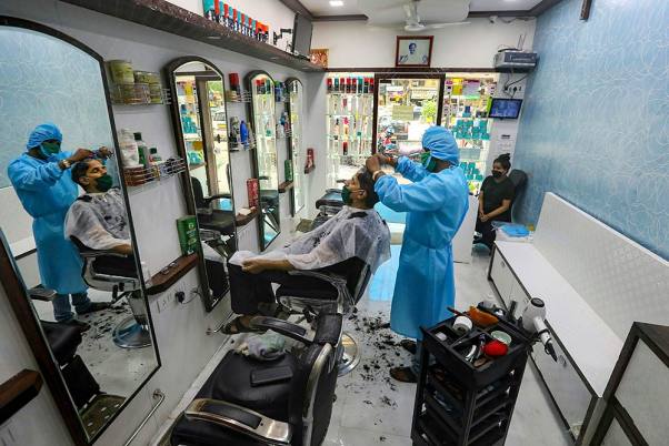मुंबई में कोविड-19 महामारी के कारण तीन महीने के बाद खोले गए सैलून में सुरक्षात्मक सूट पहने ग्राहकों के बाल काटता हेयर-स्टाइलिस्ट