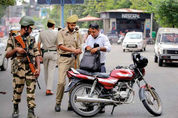 जम्मू में सुरक्षा जांच के दौरान एक मोटर साइकिल चालक के सामान का निरीक्षण करता पुलिसकर्मी