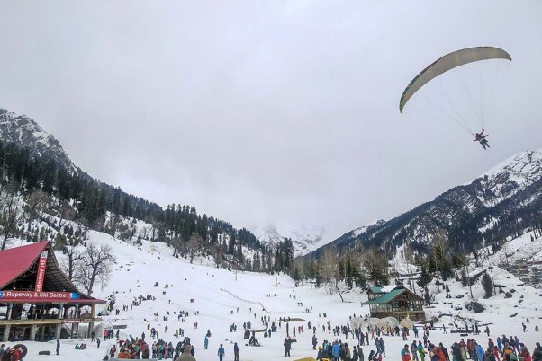 मनाली के सोलंग नाला में बर्फ से ढके पहाड़ों  के बीच उड़ता एक पैराग्लाइडर