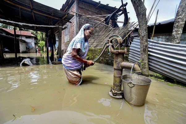 असम के कामरूप जिले में भारी बारिश के बाद बाढ़ वाले क्षेत्र में पीने के पानी के लिए जद्दोजहद करती महिला