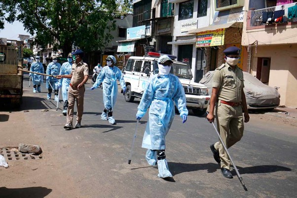 अहमदाबाद में कोरोना वायरस के प्रसार को कम करने के लिए लॉकडाउन के दौरान सुरक्षात्मक किट पहनकर सड़कों पर गश्त लगाते सुरक्षाकर्मी