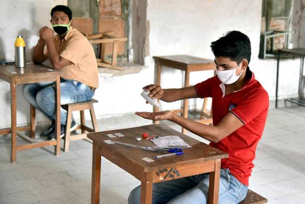 बीकानेर में लॉकडाउन के बीच 12वीं कक्षा की परीक्षा में बैठने के दौरान अपने हाथों को सेनिटाइज करता एक छात्र