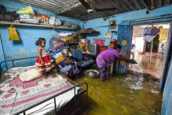 चेन्नई में भारी बारिश के बाद घर में भरा पानी निकालने की कोशिश करती महिला