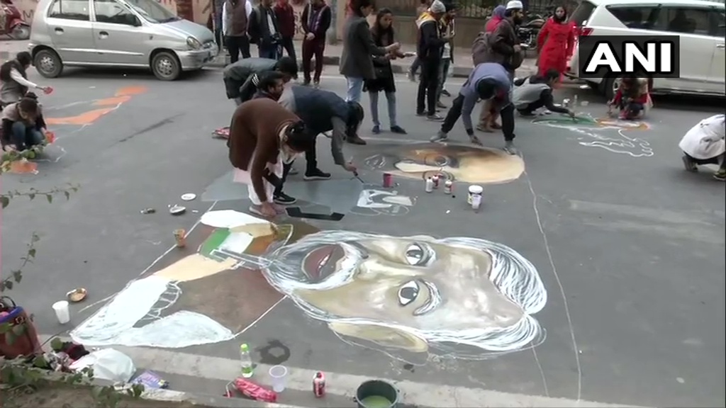 जामिया मिलिया इस्लामिया के छात्र और कलाकार सड़क पर पेंट से चित्रकारी कर सीएए और एनआरसी को लेकर विरोध जताते हुए