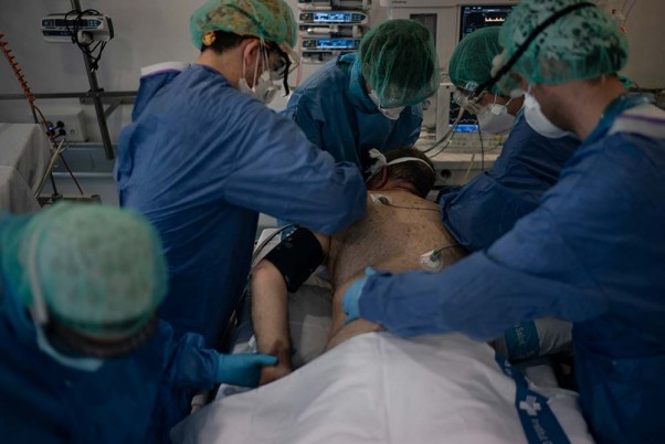स्पेन के बार्सिलोना प्रांत के एक अस्पताल की लाइब्रेरी में बनाए गए आइसीयू में एक मरीज की मदद करते स्वास्थ्यकर्मी