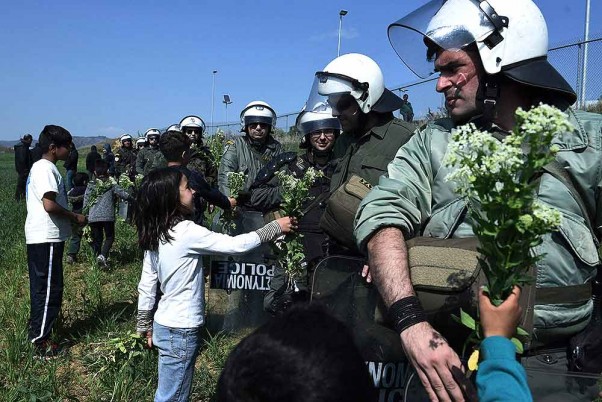 उत्तरी ग्रीस के दियावता गांव में एक शरणार्थी शिविर के बाहर एक रैली के दौरान पुलिसकर्मियों को फूल भेंट करते बच्चे