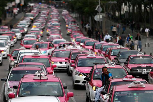 मेक्सिको सिटी में ड्राइवर के राइड-शेयरिंग ऐप्स को बंद करने की मांग के बाद टैक्सी के ऊपर बैठकर सवारी करता आदमी