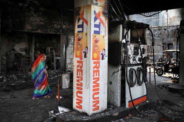 राजधानी दिल्ली में हिंसा के दौरान जले एक ईंधन स्टेशन को देखती एक महिला