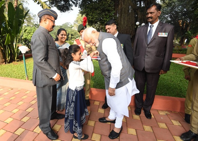 सशस्त्र सेना झंडा दिवस के मौके पर पीएम नरेंद्र मोदी के कुर्ते पर तिरंगा लगाती एक छोटी बच्ची
