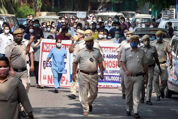 लंबित वेतन का भुगतान नहीं करने पर उत्तरी दिल्ली नगर निगम के खिलाफ विरोध प्रदर्शन करते के हिंदू राव अस्पताल के डॉक्टरों और नर्सों के साथ खड़े पुलिसकर्मी