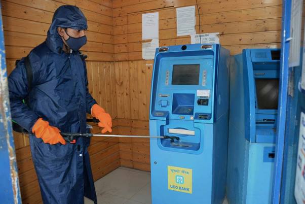 श्रीनगर में कोरोनोवायरस महामारी के प्रसार को रोकने के उपाय के तौर पर एटीएम बूथ के भीतर कीटाणुनाशक स्प्रे करता नगरपालिका कार्यकर्ता