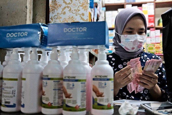 इंडोनेशिया के जकार्ता में एक मेडिकल की दुकान पर हैंड सैनिटाइजर की बोतलों के पीछे पैसे गिनती कैशियर