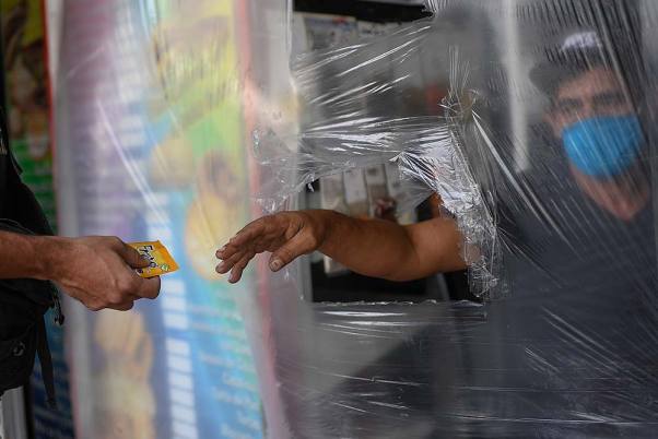 कोरोना वायरस के बढ़ते मामलों के मद्देनजर एहतियात के तौर पर वेनेजुएला के काराकस में प्लास्टिक के पर्दे के पीछे से काम करता कैशियर
