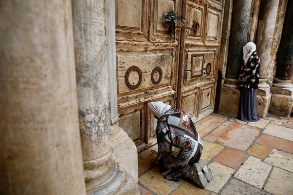 कोरोना वायरस के मद्देनजर यरूशलम के पुराने शहर में बंद चर्च के सामने बैठकर प्रार्थना करती एक महिला